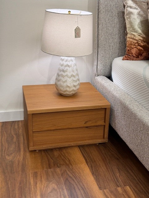 2 drawer Wooden nightstand with a lamp on top next to a bed