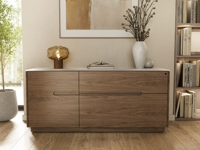 Luma 6720 Cabinet in natural walnut with dune top in decorated room with bookshelves, lamp, and potted plants.