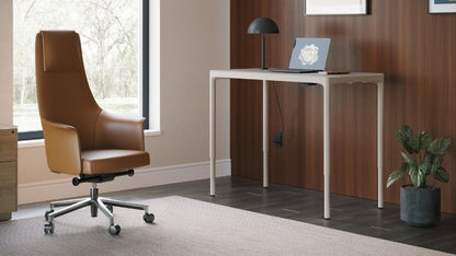 Luma Small Sit/Stand Desk in Dune at standing height in a decorated room with office chair, filing cabinet, and laptop.