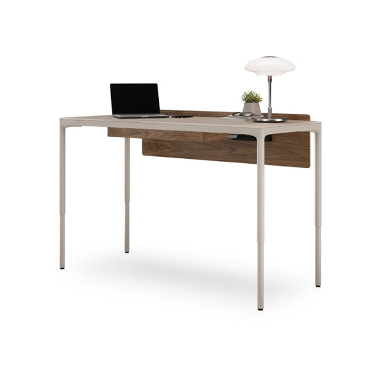 Luma Medium Sit/Stand Desk in Dune with Walnut modesty panel at standing height with laptop and lamp