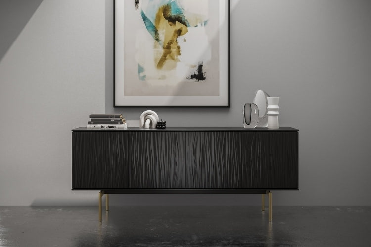Modern black sideboard with wavy texture look with brass legs with books and decorative items on top and 1 picture above it. 