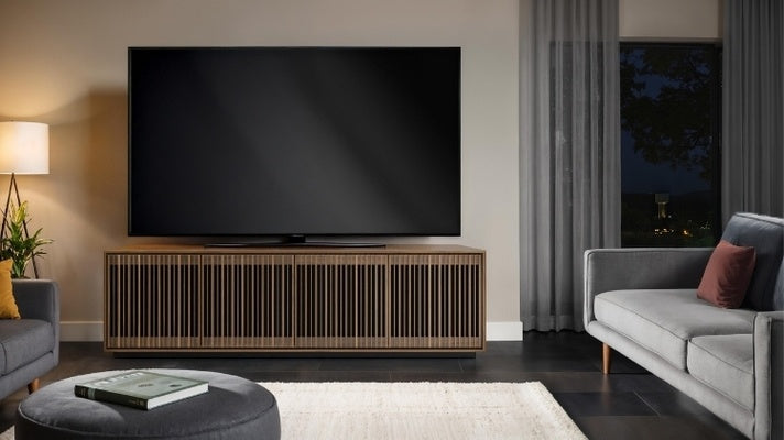 Modern living room with a large TV on a wooden stand, gray sofa, and ottoman.