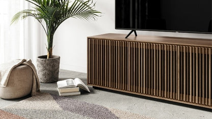 Wooden TV stand with a television, books, and a plant in a living room setting.