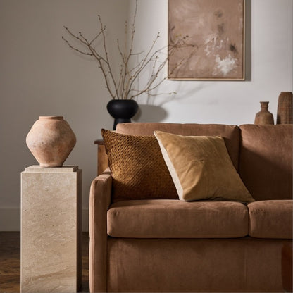 Brown sofa with decorative pillows in a room with vases and a painting.
