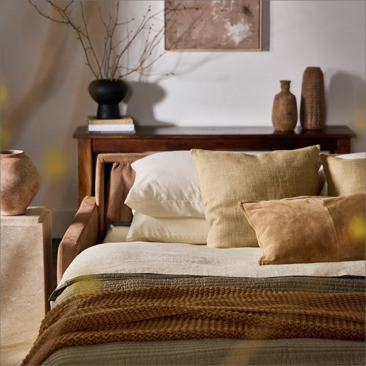 Cozy bedroom with a bed featuring beige pillows and a blanket, wooden side table with decorative items.