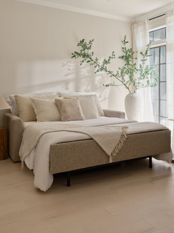 Beige sofa with cushions and a blanket in a bright room with large windows.