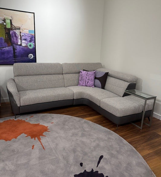 Gray sectional sofa with colorful cushions in a room with a round rug and abstract painting.