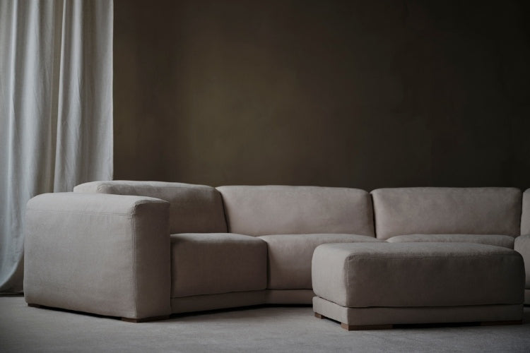 Beige sectional sofa in a minimalistic room with a dark wall and light curtain.
