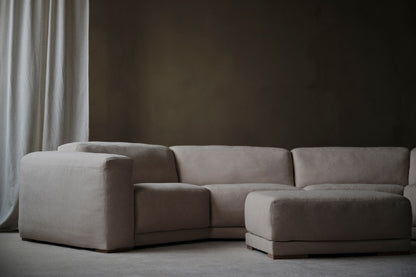 Beige sectional sofa in a minimalistic room with a dark wall and light curtain.