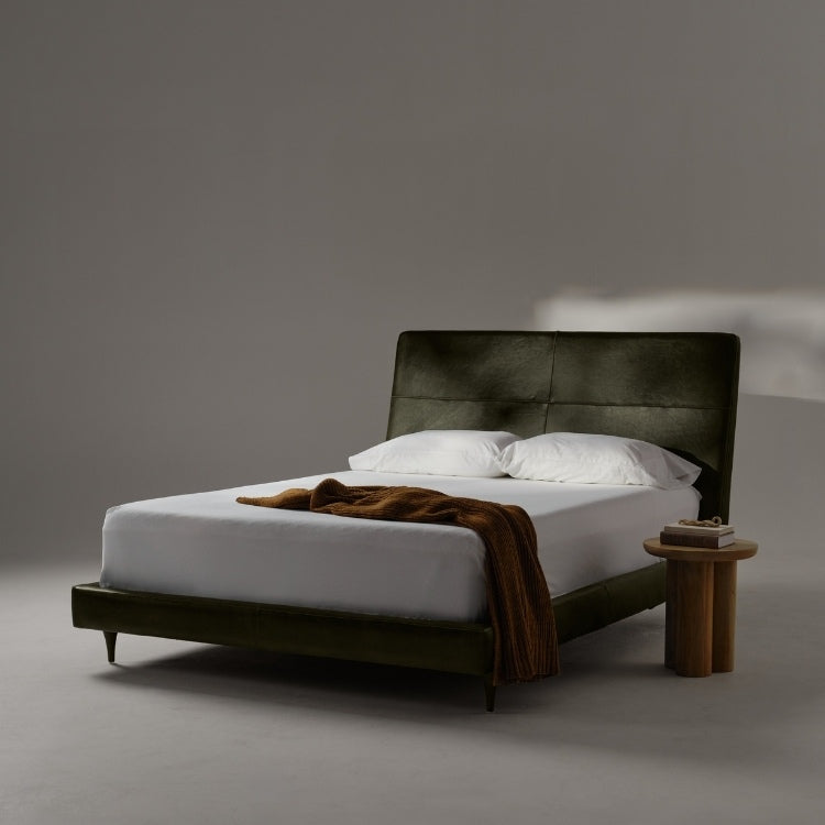 Menlo Park Bed Reimagined Green Leather Upholstered with white bedding and pillows and side table with books.
