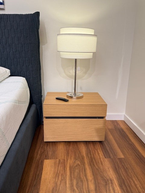 Wooden nightstand with a lamp next to a bed in a bedroom.