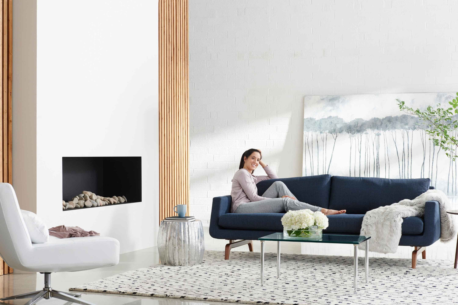 Woman sitting on a blue American Leather sofa in a modern living room with a fireplace and large windows.