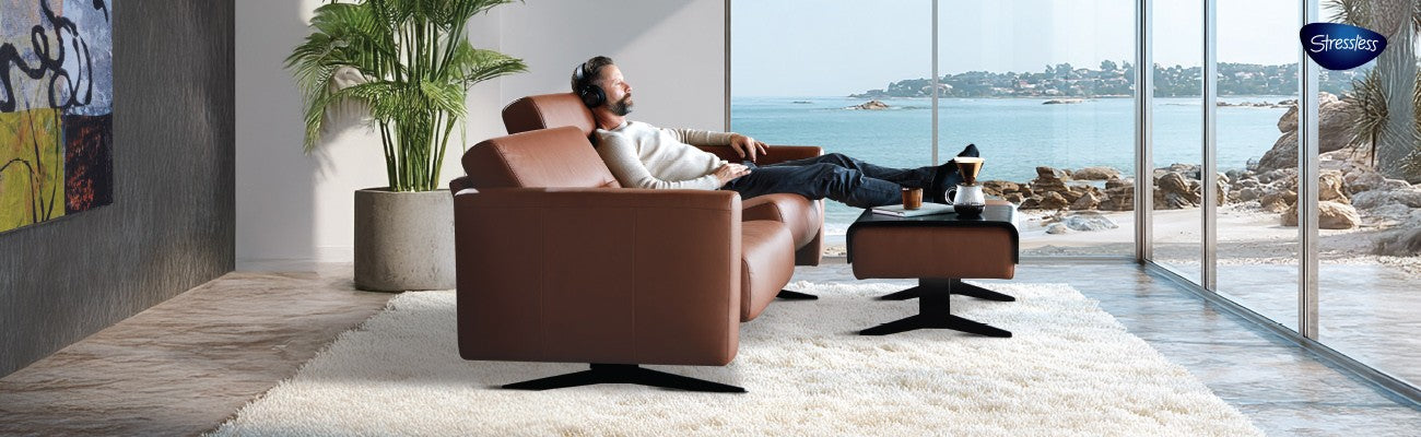 Man relaxing on a Comfortech sofa in a modern living room with a scenic view.