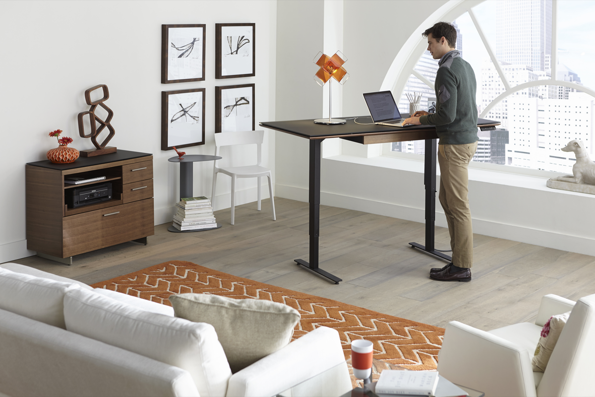 Office staging of the Sequel 20 6152 Lift Desk by BDI Furniture in Chocolate Stained Walnut, featuring a man at work.