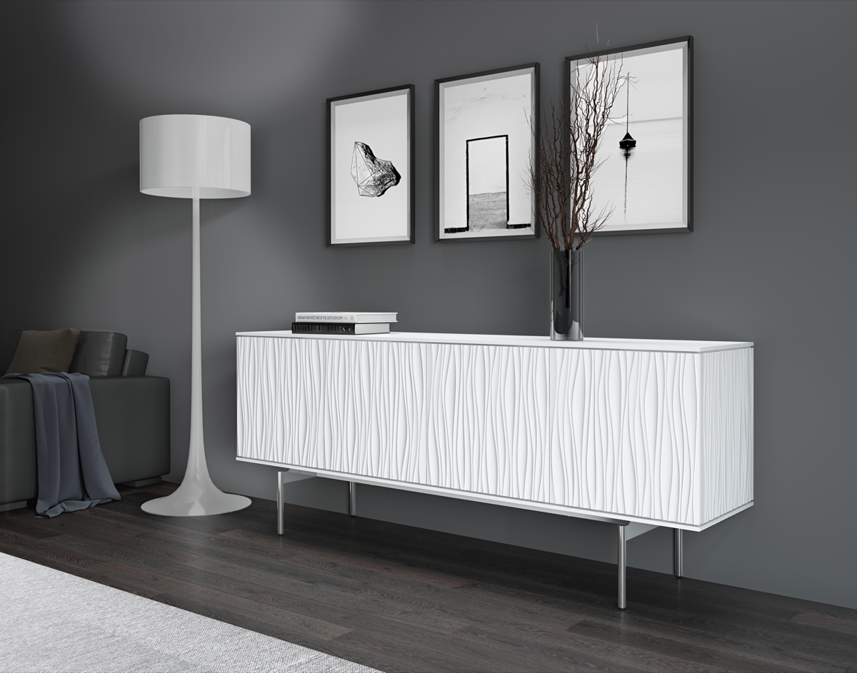 White sideboard with with stainless steel legs and 2 books a vase on top with 3 pictures on the wall and tall white lamp. 